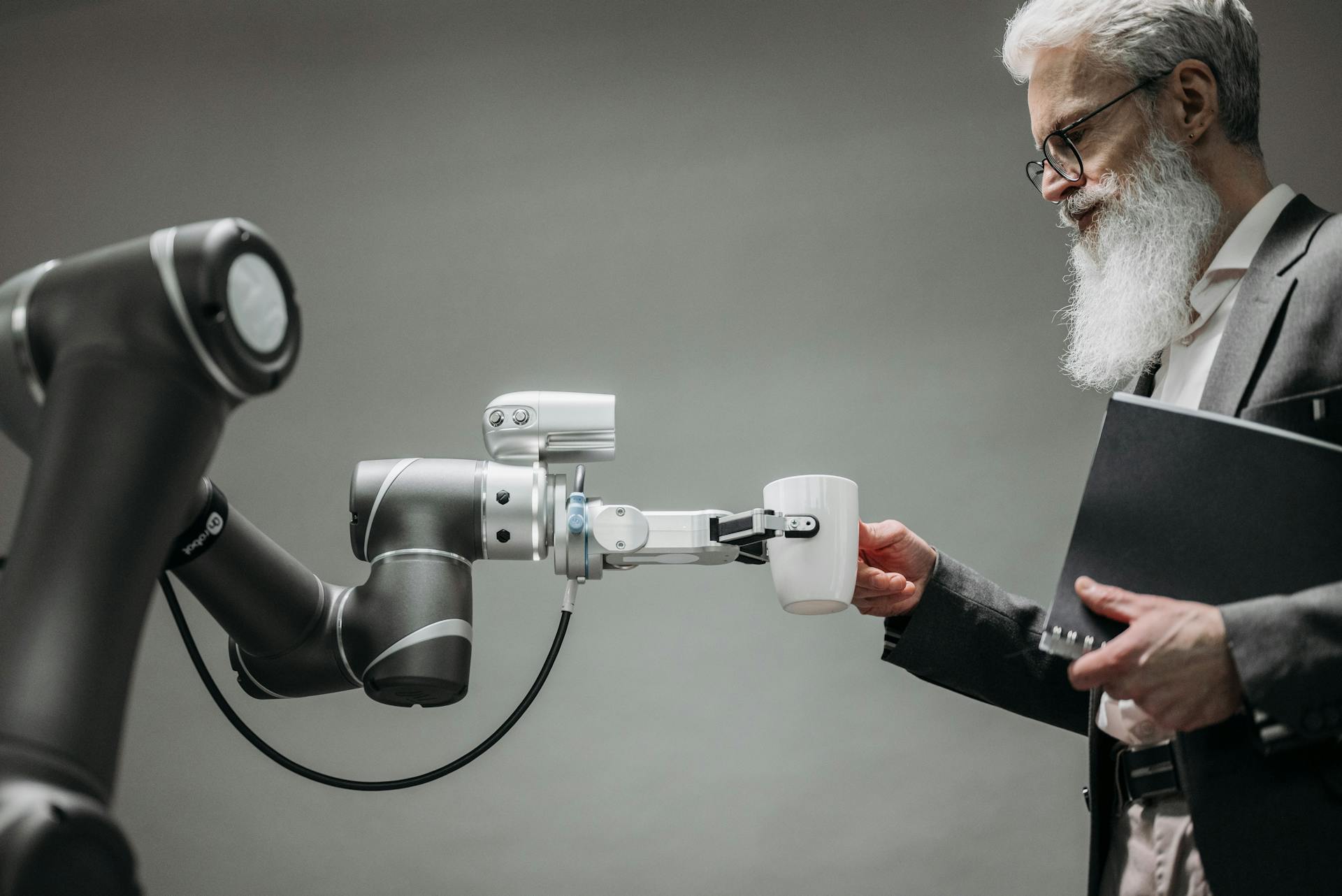 A robotic arm hands a mug to an older man