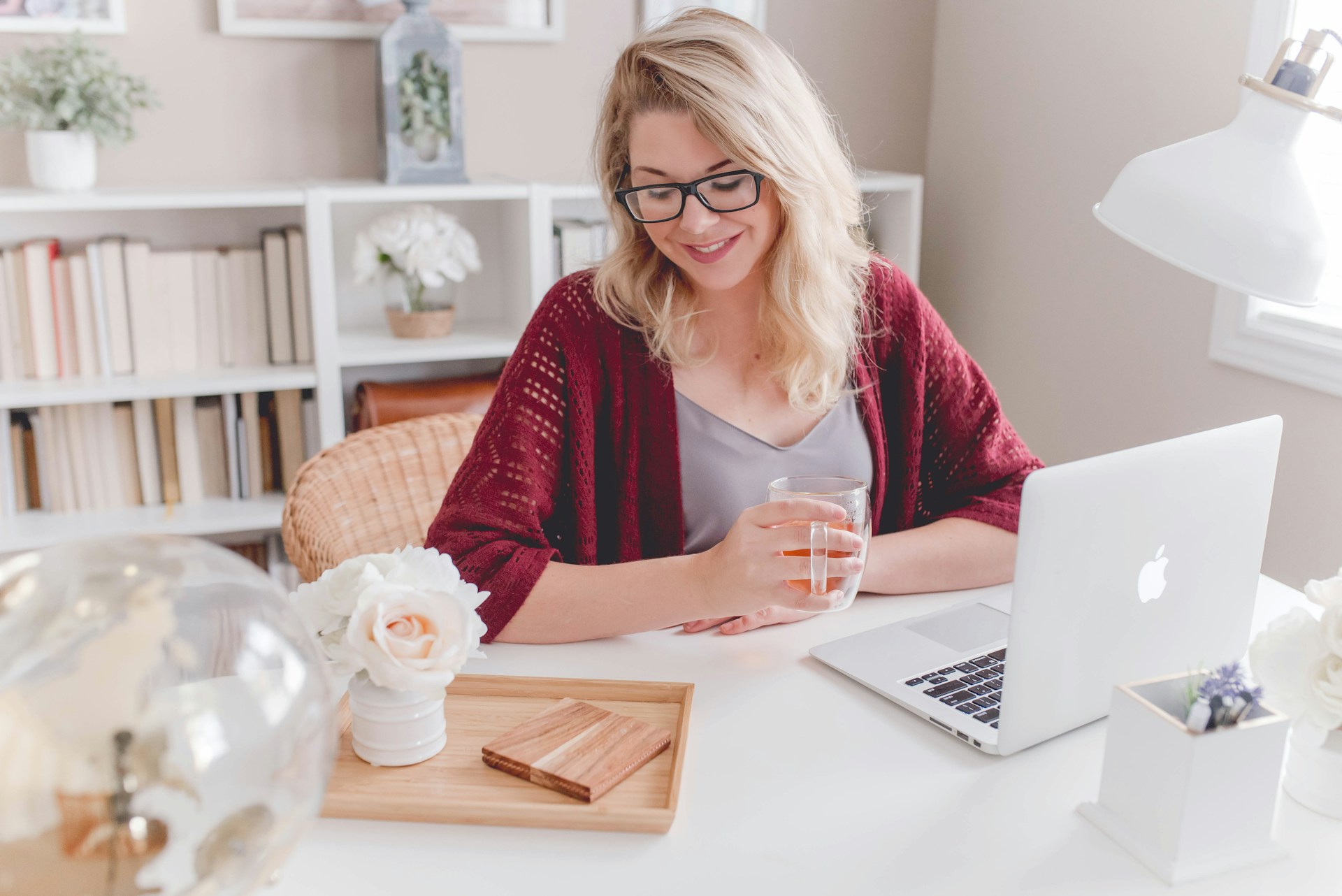 woman-smiling-holding-glass-mug-sitting-beside-table-with-macbook